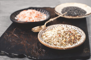 different types of salt. Three different types of salt in handmade plates on a clay board. White spiced salt, pink Himalayan salt and black Maldon salt.
