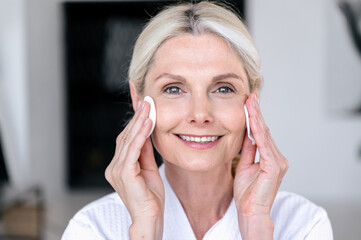 Mature woman looking at camera, holding white cotton pad near face