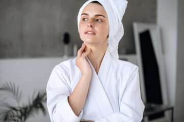 Woman in bathrobe standing in bathroom and touching neck