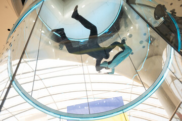 Excited teenage girl in helmet flying in aerodynamic tube wind tunnel. Skydiving training.