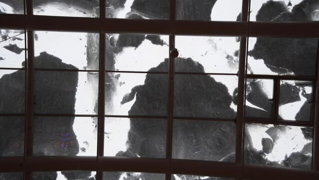 Low angle view of thick snow lying on building's glass roof. Overcast sky. Snow moved in different directions creates a pattern. Abstract winter natural background. Real time handheld video.
