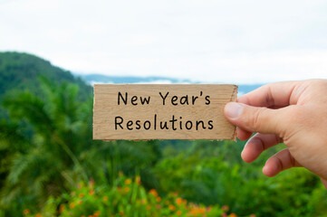 Hand holding wooden block with New Year's Resolution text with beautiful nature background