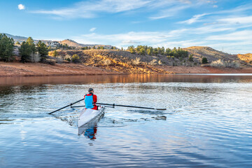 Senior male rower is rowing a coastal rowing shell - Horsetooth Reservoir in fall or winter scenery...