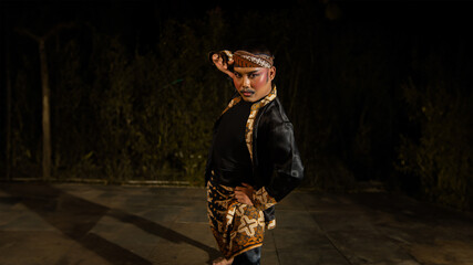 an Indonesian man dances with determination and skill while wearing a black costume on stage