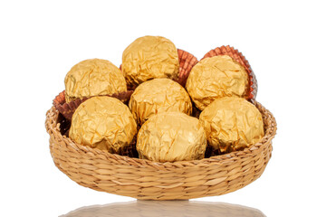 Several chocolates in a paper wrapper on a straw plate, macro, isolated on a white background.