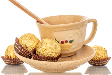 Several chocolates in a paper wrapper on a ceramic saucer with a cup, macro, isolated on a white background.