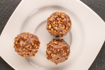 Several chocolates with white ceramic saucer on slate stone, macro, top view.
