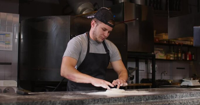 Caucasian chef baker touching raw dough with his hands. Young chef preparing dough for baking. Mixing flour and shaping dough. Occupation. Working at kitchen. Concept of culinary.