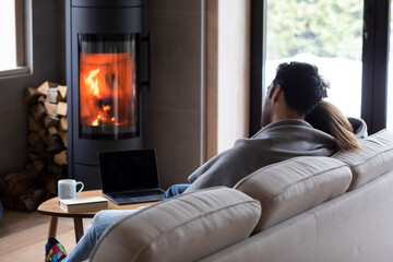 Back view on cute lovers sitting on the couch close to fireplace. Young couple spending time...