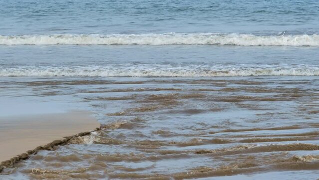 Close up of the choppy coastline with brown sand meeting the flowing water of the estuary