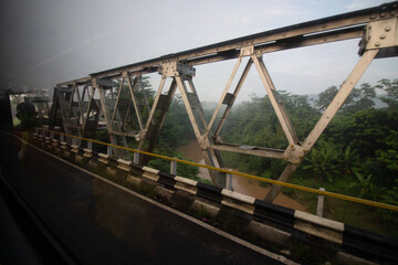 View of a metal truss bridge from a moving vehicle on a misty day.