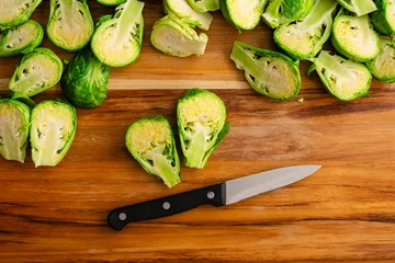 Fotobehang Halved Brussels Sprout Viewed Close Up on a Wood Cutting Board: Fresh brussels sprouts halved with a paring knife on a wooden carving board © Candice Bell