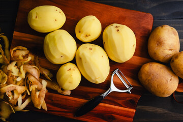 Peeled Yukon Gold Potatoes on a Wooden Cutting Board: Peeled and unpeeled golden yellow potatoes...