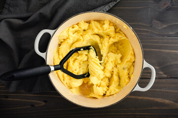 Mashing Boiled Yukon Gold Potatoes in a Large Pot: Potato masher and golden yellow potatoes in an enameled cast-iron Dutch oven 