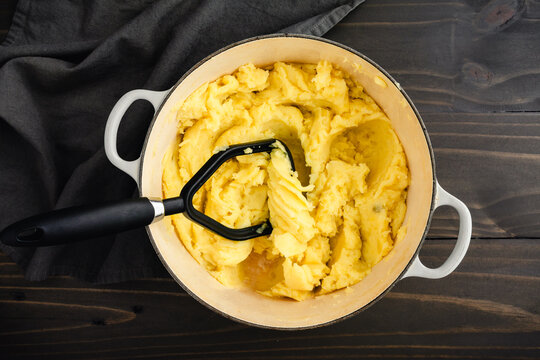 Mashing Boiled Yukon Gold Potatoes in a Large Pot: Potato masher and golden yellow potatoes in an enameled cast-iron Dutch oven 