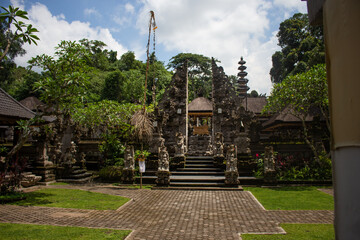 A tranquil scene at a Balinese temple courtyard with traditional architecture, shrubbery, and...