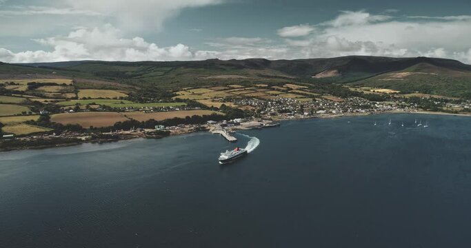 Tourist cruise liner (ferry, passenger ship, motor ship,) departs from shores (coast) of Scotland. Aerial view: Scottish landscape - greenery valley and mountains. Brodick Terminal, Arran Island