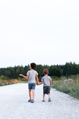 Fototapeta premium Two boys, two brothers or two friends, are walking along the road hugging and talking. The picture was taken from the back. High quality photo