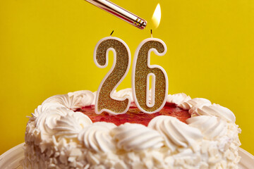 A candle in the form of the number 26, stuck in a festive cake, is lit. Celebrating a birthday or a...