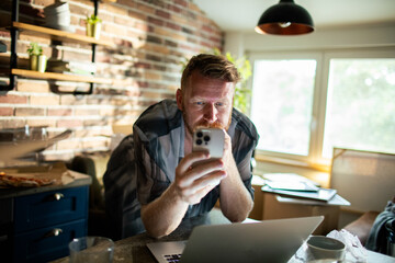 Focused man multitasking with a smartphone and laptop at home