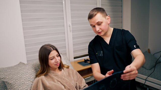 the doctor shows a picture of a brain tomography to a sick patient in the hospital and tells about the treatment plan