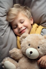 boy sleeps sweetly in bed with a toy bear in his arms under the blanket