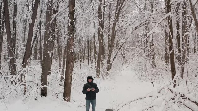 Winter forest, a man films winter from a helicopter. A man takes pictures of a snow-covered forest on a smartphone. A young man with a camera smiles while standing in a snowy forest.