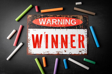 Winner. Metal warning sign and colored pieces of chalk on a dark chalkboard background