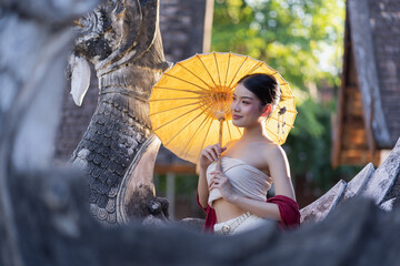 Young beautiful Asian woman wearing thai traditional dress holding umbrella in hand walking at ancient temple with old pagoda in Chiang Mai, Thailand