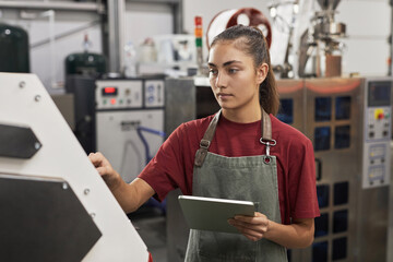 Waist up portrait of young female worker using touch screen control panel while operating machines in food factory workshop, copy space - obrazy, fototapety, plakaty