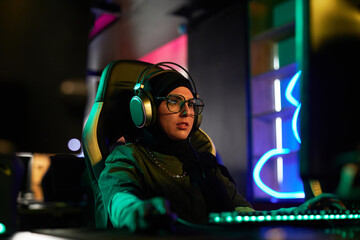Portrait of Muslim young woman playing videogames in neon light and wearing headphones, cyberpunk...