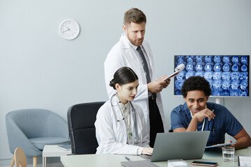Multiethnic group of doctors using laptop and looking at X-ray images together in clinic, copy space