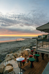 Labradoodle dog stands under a party heater on the beach deck overlooking the Pacific Ocean at sunset
