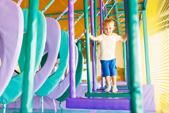 Cute little boy crawling and playing on colorful playground at amusement park