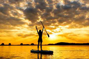 silhouette of woman on inflatable SUP board and paddling through shining water surface....