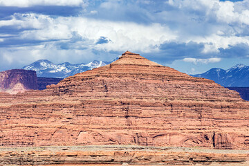 Pyramid Butte in the arid, desert landscape of Canyonlands National Park Utah with the La Sal Mountains and cloudy blue sky in the background.