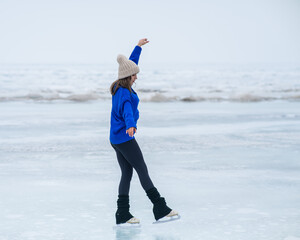 Caucasian woman in a blue sweater is skating on a frozen lake. The figure skater performs the...