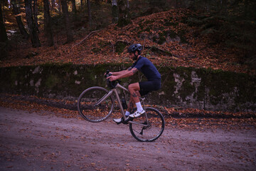 Man cyclist on gravel bicycle riding wheelie on a rear wheel in forest. Cyclist practicing on...