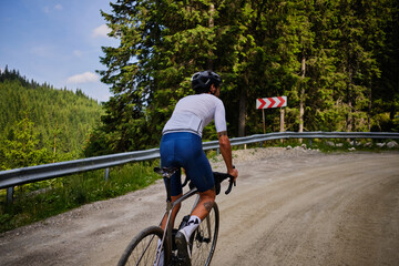 Man cyclist wearing cycling kit and helmet riding gravel bike on gravel road in mountains with...