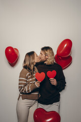 Loving couple holding heart shape Valentines cards and kissing with balloons flying around