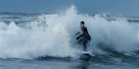 Woman in wetsuit surfing the arctic cold waves. Lofoten, Northern Norway. 