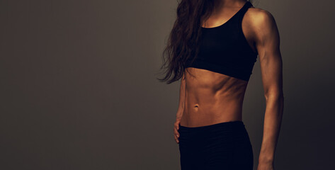 Sport muscular woman posing in black sport bra showing  abs and arms, standing on dark shadow...