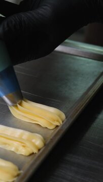 A pastry chef makes eclairs in a bakery. eclairs are baked in the oven. eclair production process. pastry bag with dough