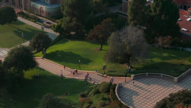 Aerial view of UCLA campus bathed in golden light, showcasing Romanesque Revival and Gothic architecture amid lush greenery, with Royce Hall as the centerpiece.