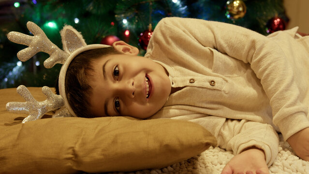 Cute boy sleeping near the christmas tree opening eyes and gets surprised. High quality photo