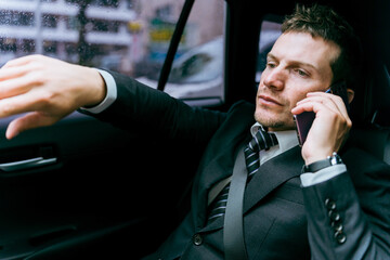 タクシーに乗ってスマホで話しながら行き先を指示する乗客の欧米人ビジネスマン
 - obrazy, fototapety, plakaty