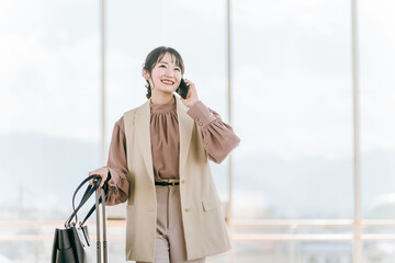 駅ビル・デパート・空港・公共交通機関でスマホで電話する若い女性・旅行するアジア人ビジネスウーマン

