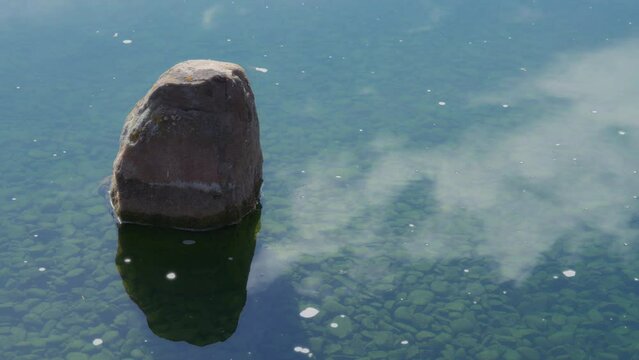 Big rock surrounded by water surface and reflecting clouds in summer. Slow motion. 