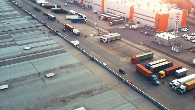 Aerial view of a logistics park with warehouses. Semi-trailer truck drives along ramps with a lot of cargo containers standing for unloading and loading goods