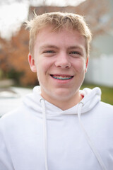 Portrait of smiling blonde teenage boy wearing a hoodie sweatshirt with braces on his face. Authentic Real people concept photo
